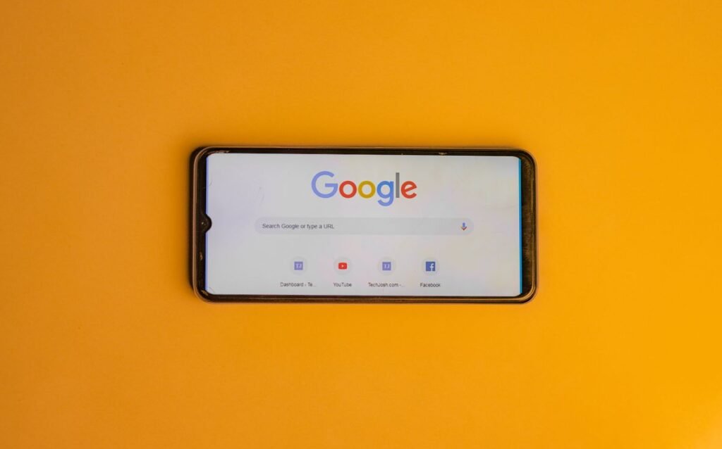 Smartphone displaying Google search page on a vibrant yellow background.