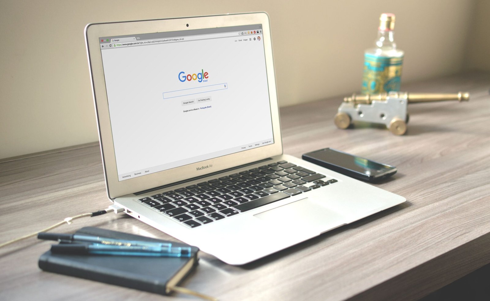 A neat workspace featuring a laptop displaying Google search, a smartphone, and a notebook on a wooden desk.